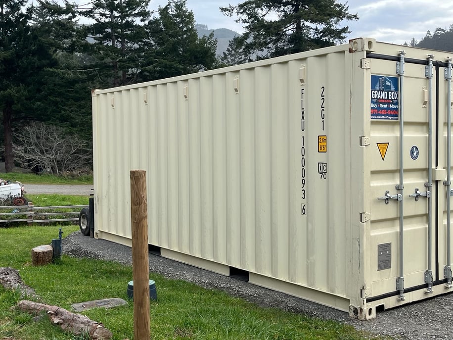 Beige shipping container installed on a gravel pad in a rural setting - Grand Box Northwest