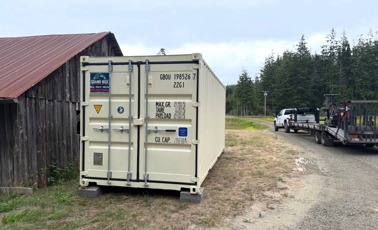 Beige steel shipping container beside a building on a gravel lot
